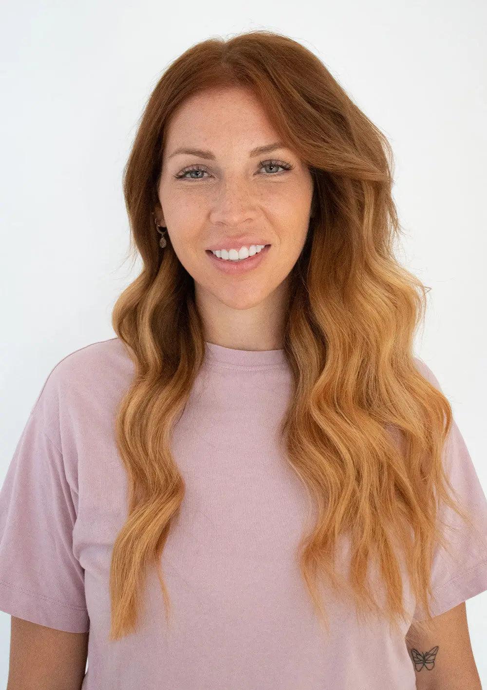 Stylish woman with long, wavy hair wearing a pink shirt against a light background, showcasing healthy hair.