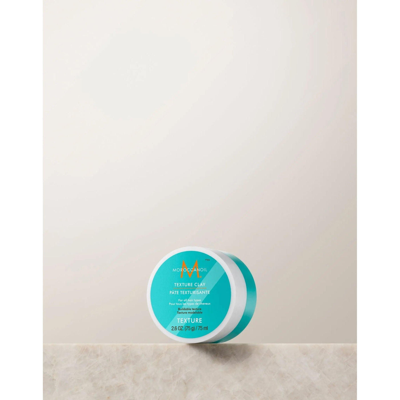 Moroccanoil Texture Clay in a round container, perfect for sculpting hair with a matte finish and strong hold.