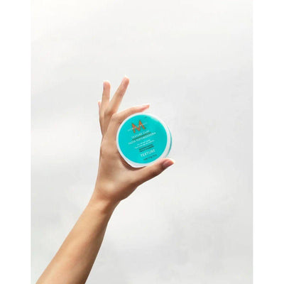 Moroccanoil Texture Clay held in a hand, showcasing its turquoise packaging for sculpting and defining hair styles.