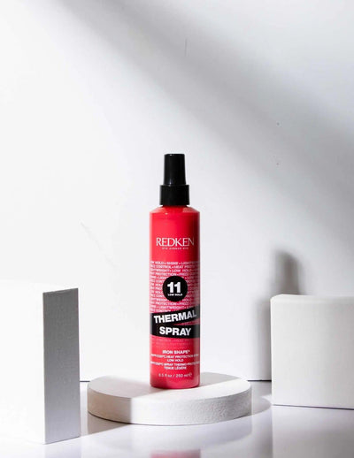 Redken Thermal Spray 11 Low Hold on a white display podium, designed for heat protection and flexible styling.