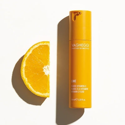 Lime Vitamin C Fluid skincare product beside a fresh orange for hydration and skin rejuvenation. 50ml bottle.