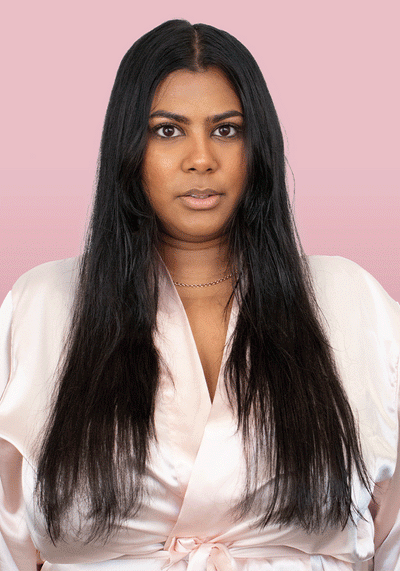 Woman with long, straight hair wearing a satin robe against a pink background, showcasing shiny, healthy hair.