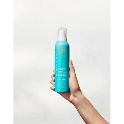 Moroccanoil Volumizing Mousse bottle held in hand, designed for instant volume and lift in fine hair.
