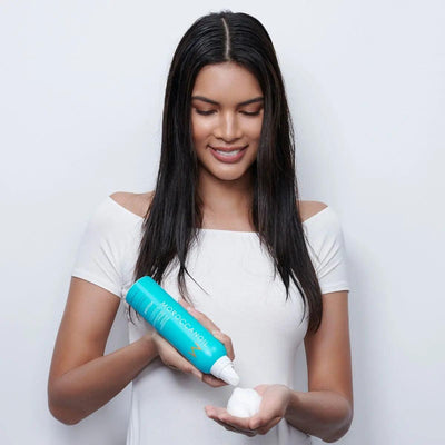 Model applying Moroccanoil Volumizing Mousse for medium to fine hair, showcasing its lightweight formula and instant volume.