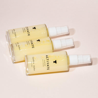 Three bottles of Activate facial spray laying on a beige background.