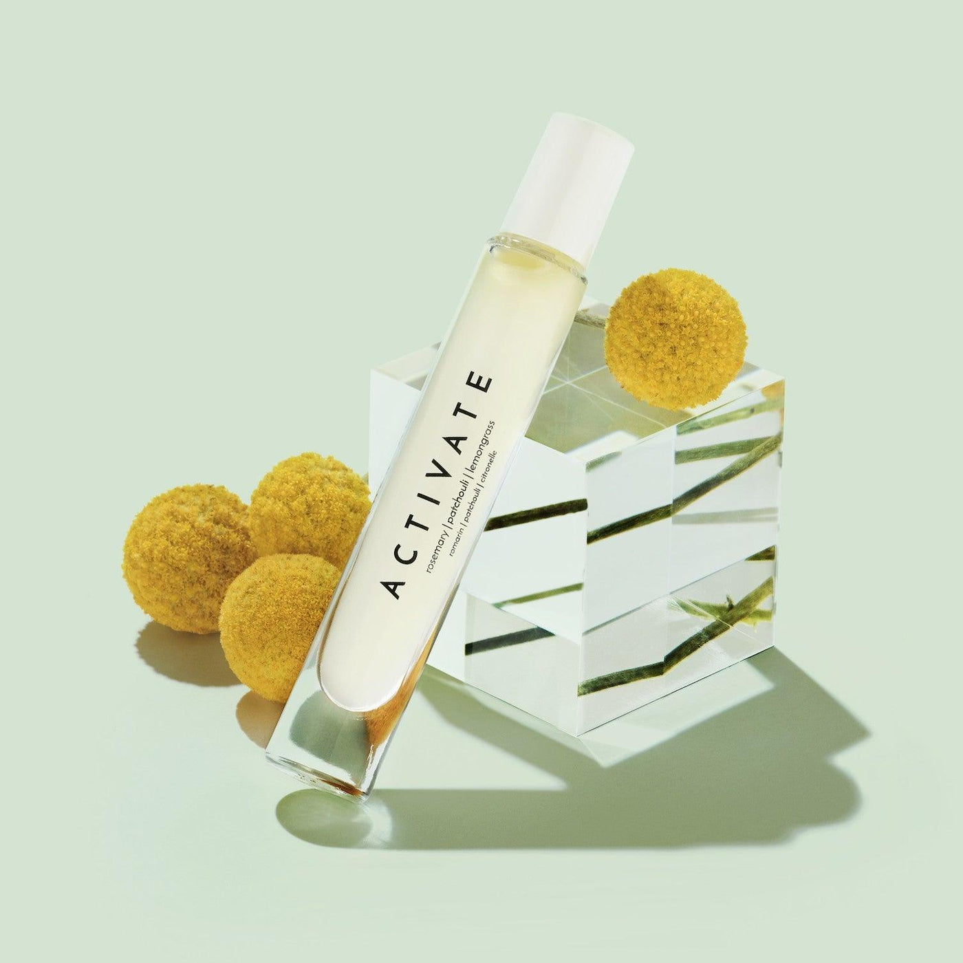 Activate essential oil bottle with yellow pompom flowers on a green background in a minimalistic setting.