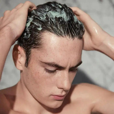 Young man applying Kerastase Argile Équilibrante Purifying Clay Shampoo to balance oily hair and scalp.