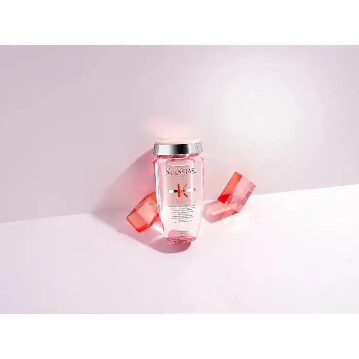 Kerastase hair product bottle with pink geometric shapes behind on white background