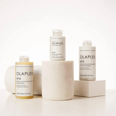 OLAPLEX Bond Maintenance System Kit featuring No.3 Hair Perfector, No.4 Shampoo, and No.5 Conditioner on a neutral background.