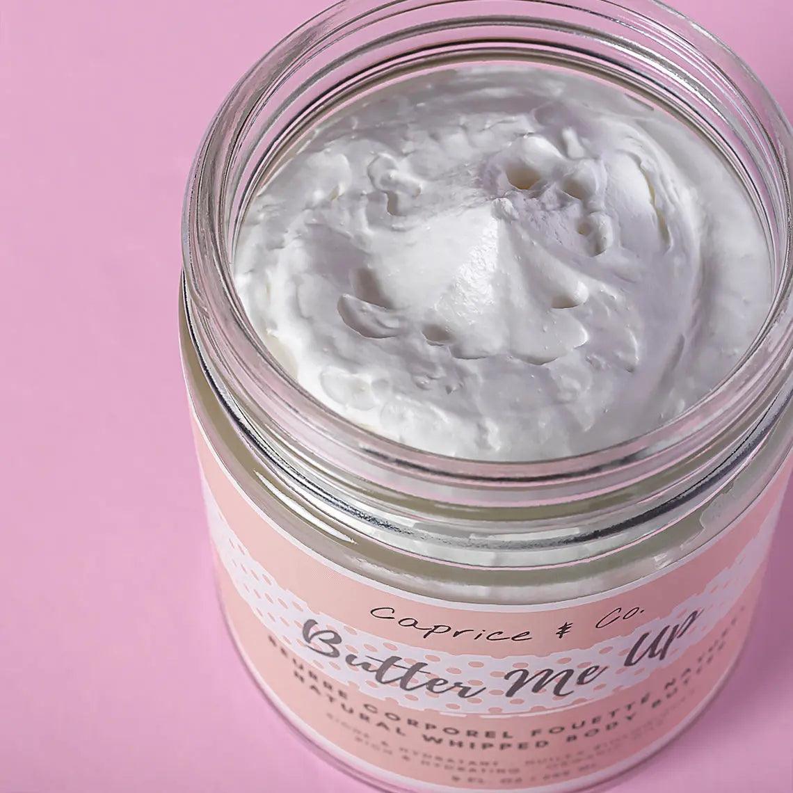 Butter Me Up natural whipped body butter with rich white freesia and vanilla scent in a glass jar on a pink background.