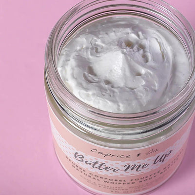 Butter Me Up natural whipped body butter with rich white freesia and vanilla scent in a glass jar on a pink background.