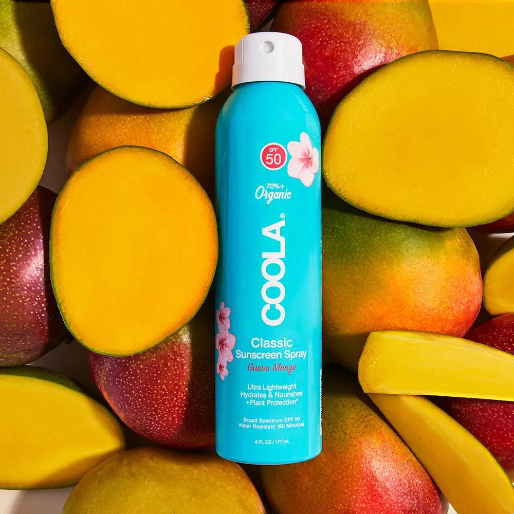Classic Body Organic Sunscreen Spray SPF 50 in Guava Mango scent on a colorful backdrop of fresh mangoes.
