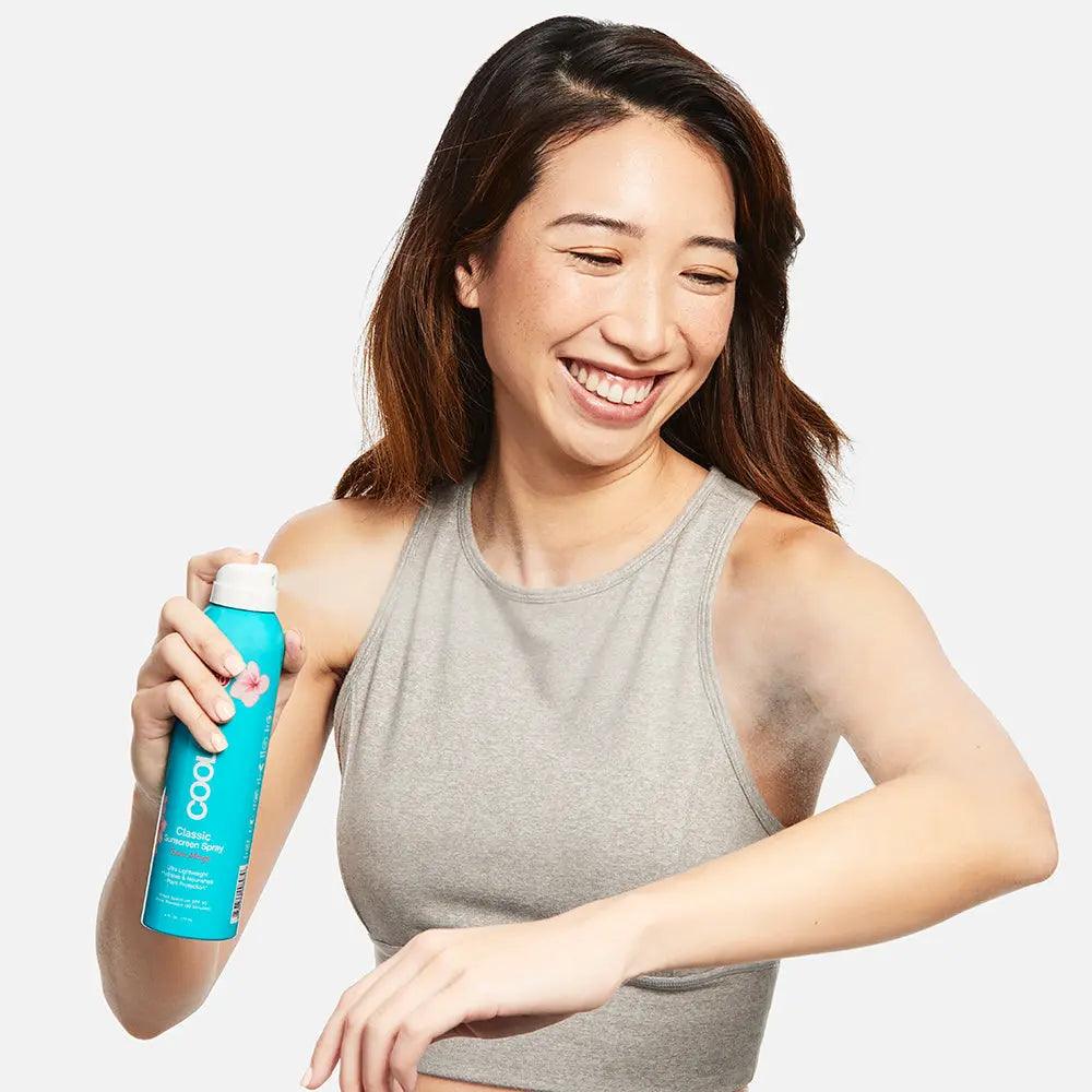 Woman applying Classic Body Organic Sunscreen Spray SPF 50 with a smile, showcasing its refreshing and light texture.