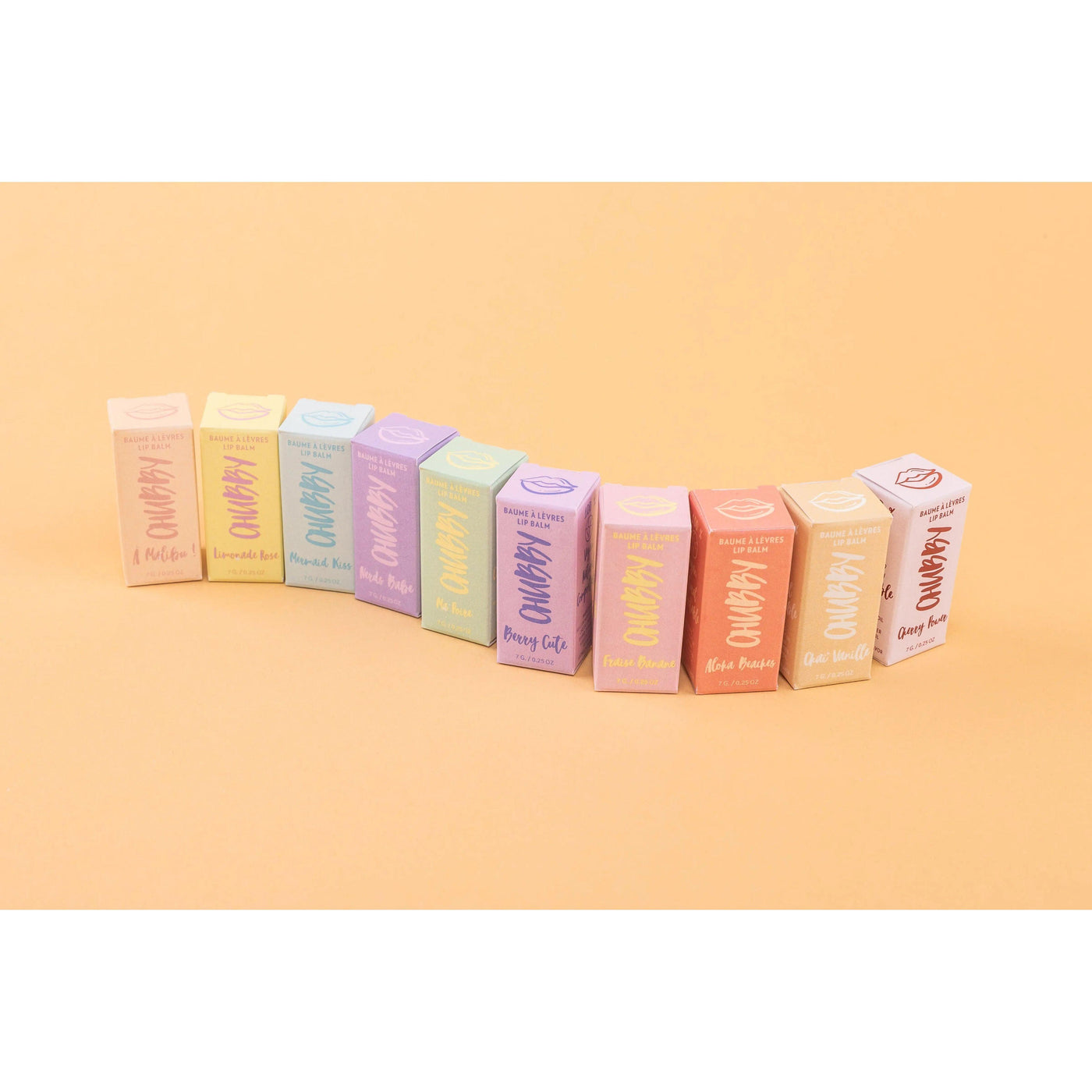 Colorful lineup of compostable vegan lip balm boxes on an orange background, showcasing eco-friendly packaging.