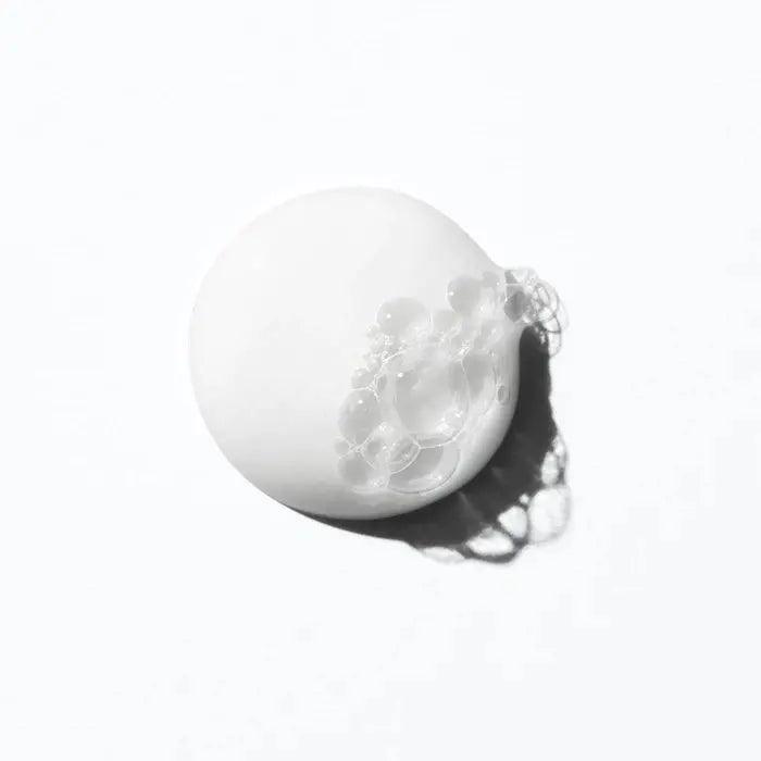 White creamy shampoo with bubbles on a light background, representing gentle hydration for curly hair.