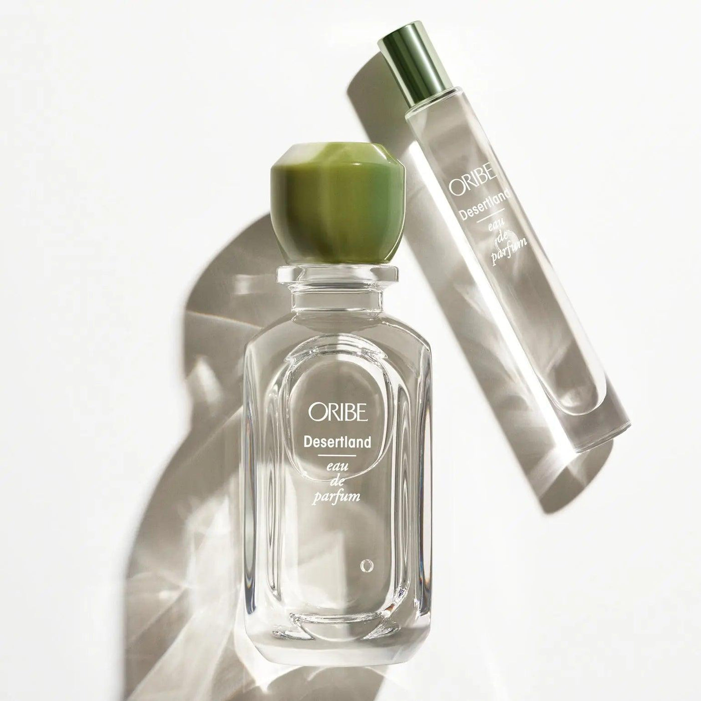 Oribe Desertland Eau De Parfum bottle and rollerball on a reflective surface, showcasing its elegant packaging.
