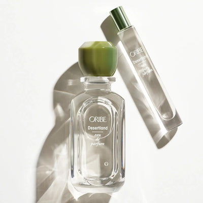 Oribe Desertland Eau De Parfum bottle and rollerball on a reflective surface, showcasing its elegant packaging.