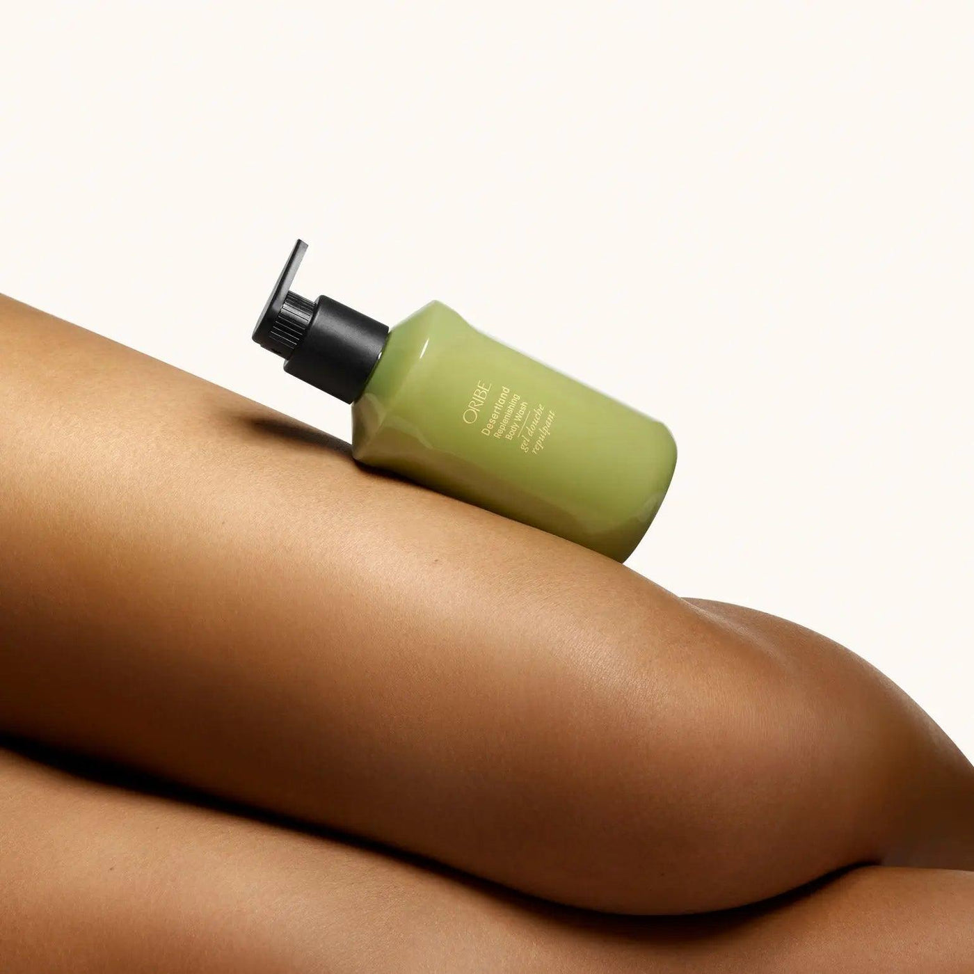 Oribe Desertland Replenishing Body Wash bottle resting on smooth skin, showcasing luxurious cleansing and hydration benefits.