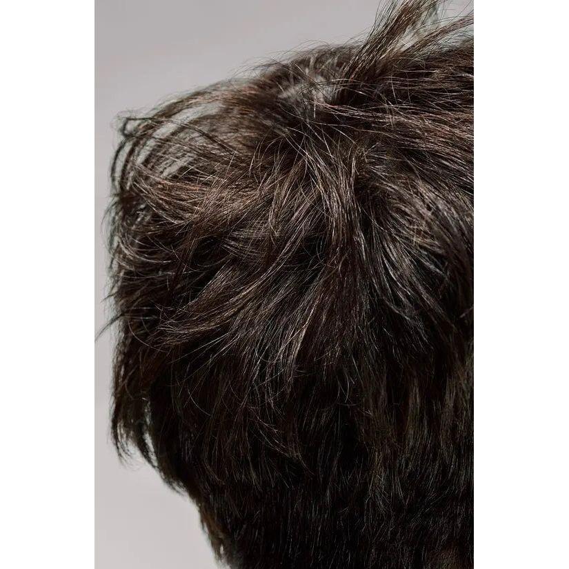 Close-up image of dark brown tousled short hair with messy layers against a grey background.