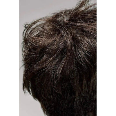Close-up image of dark brown tousled short hair with messy layers against a grey background.