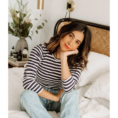 Woman with messy waves hairstyle, wearing striped top, relaxing in a cozy bedroom setting.