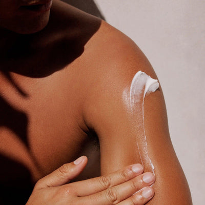 Close-up of a person applying Gilded Woods Body Lotion to their shoulder for hydration and nourishment.