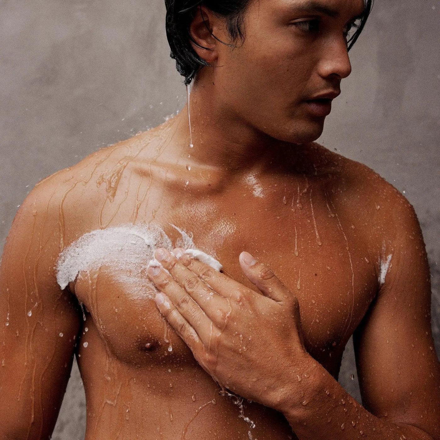 Man applying Gilded Woods Body Scrub while showering, showcasing smooth, hydrated skin with water droplets.