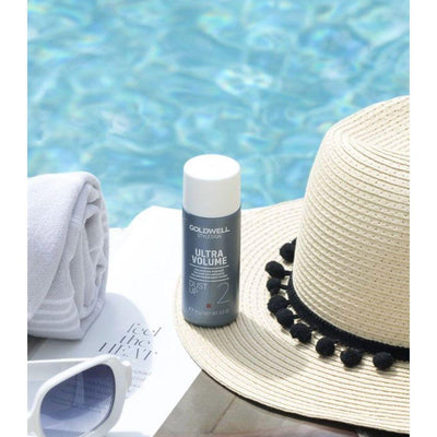 Goldwell Stylesign Ultra Volume Dust Up Volumizing Powder beside a sunhat and towel by a pool.