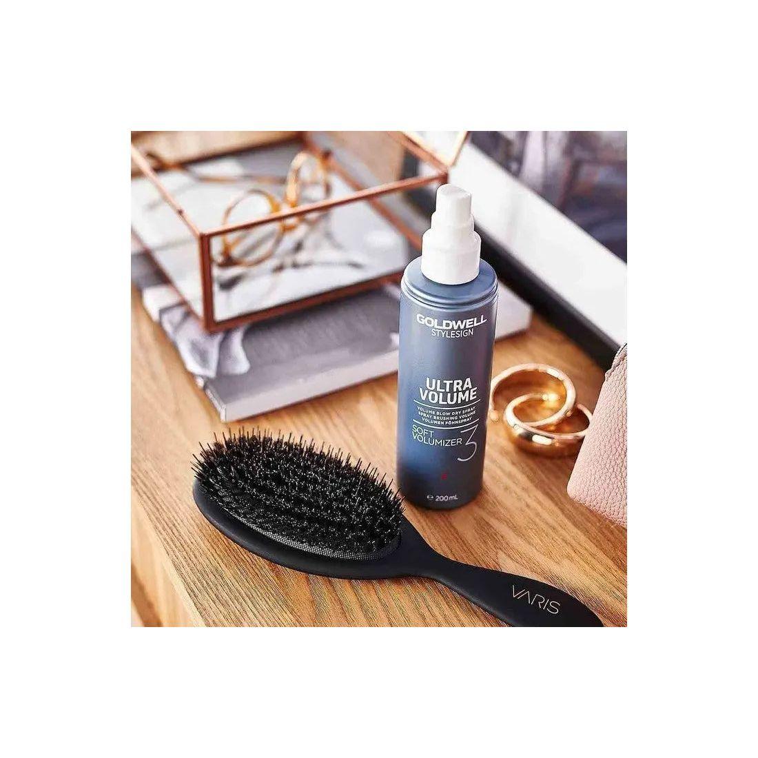 Goldwell Stylesign Ultra Volume Soft Volumizer Blow-Dry Spray with a brush on a stylish vanity table.