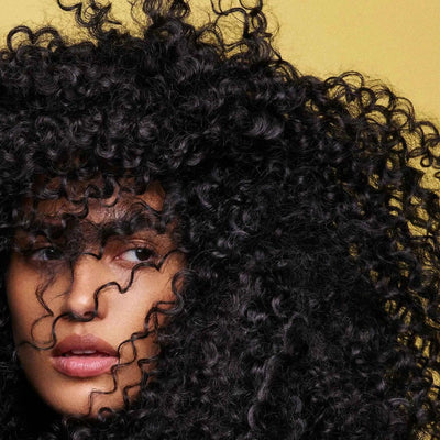 Close-up of a woman with voluminous, textured curly hair against a soft yellow background.