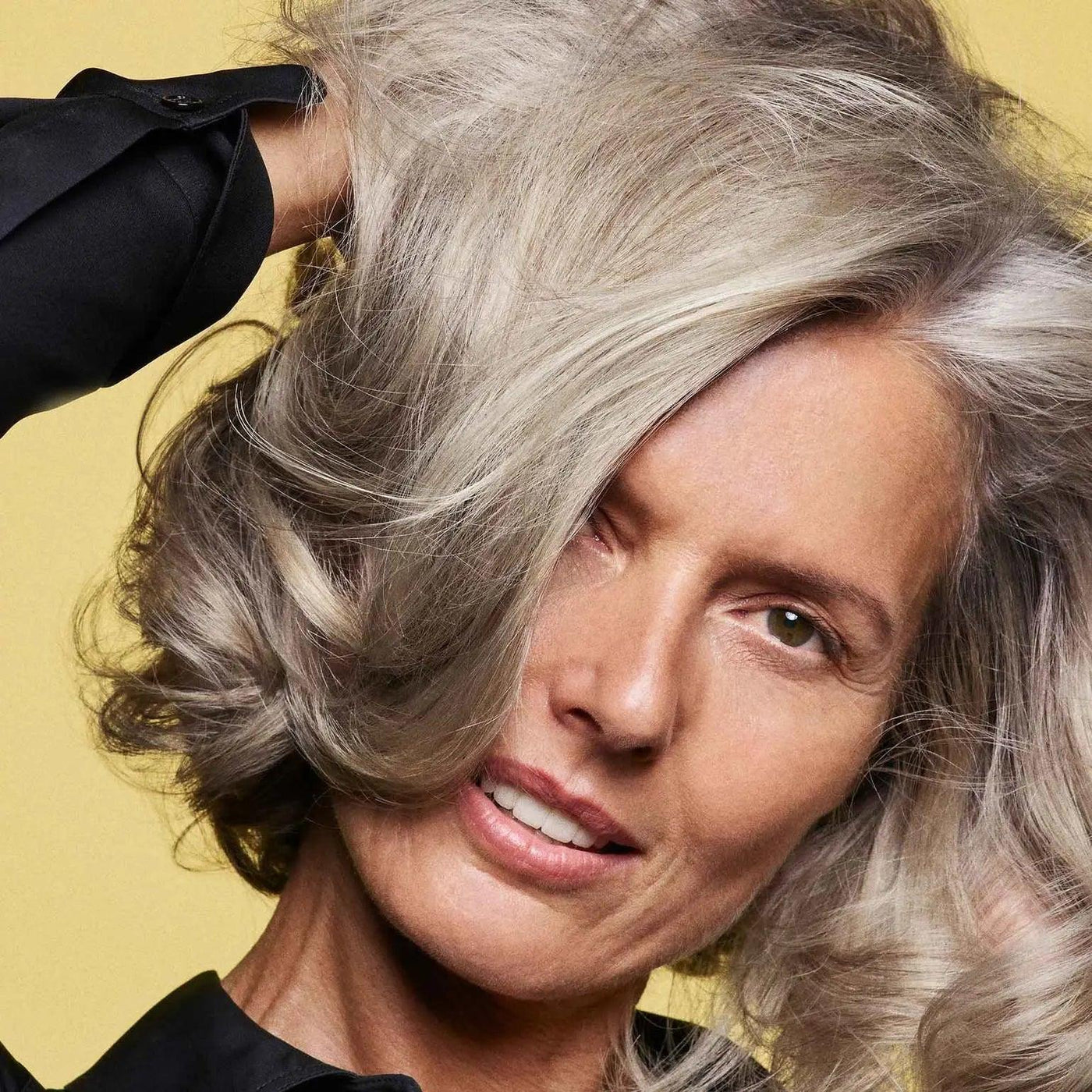 Woman showcasing healthy, voluminous gray hair, embodying strength and beauty with a confident smile.