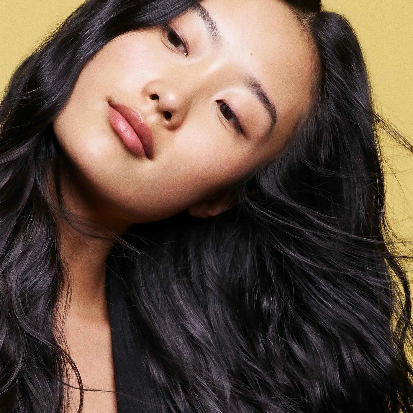 Woman with long, wavy hair, showcasing healthy locks against a vibrant yellow background.