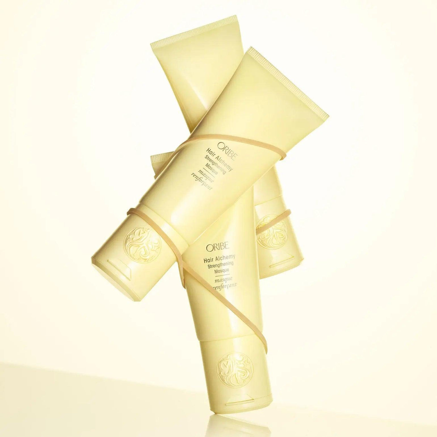 Three tubes of Oribe Hair Alchemy Strengthening Masque showcasing hydration and nourishment for fragile hair.