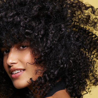 Close-up of a woman with voluminous curly hair, showcasing healthy, defined curls against a bright background.
