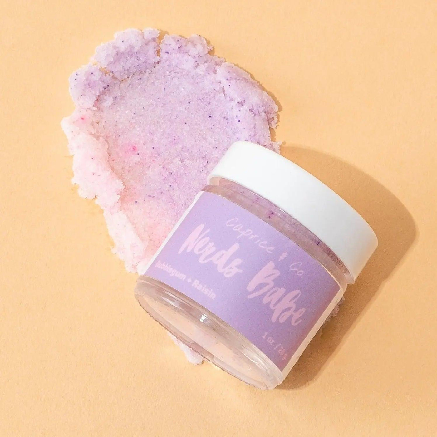 Nerds Babe lip scrub jar with bubblegum and grape flavor on a pastel background, showcasing vibrant purple hues.