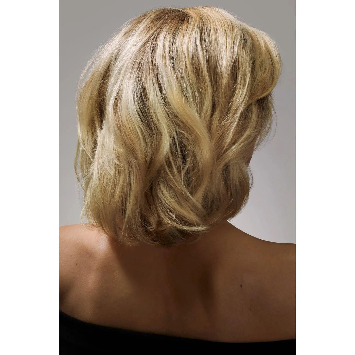 Blonde woman with shoulder-length hair seen from the back, wearing an off-shoulder black top.