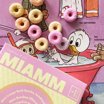 Miamm mini bath bombs in pastel colors lying on a vibrant cartoon background featuring a duck in a bathtub.