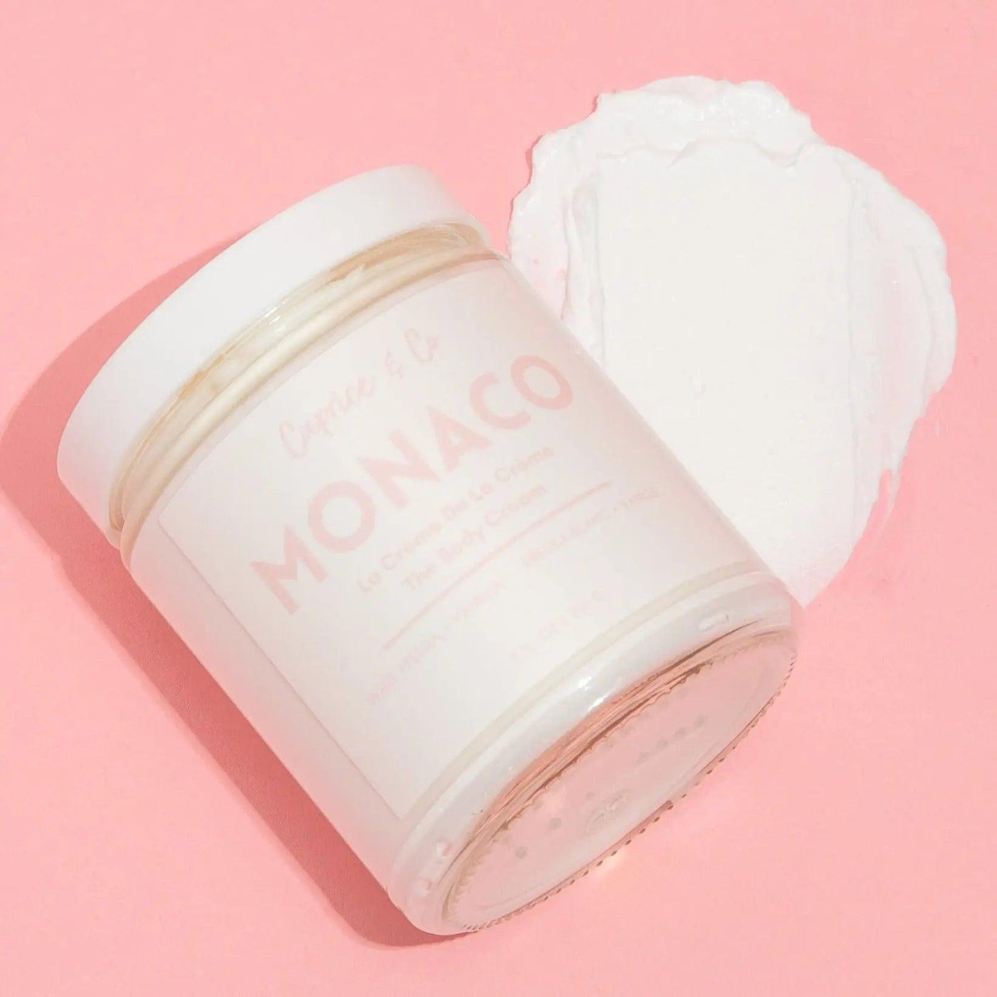 Monaco body cream jar with white freesia and vanilla scent on a pink background, highlighting its creamy texture.