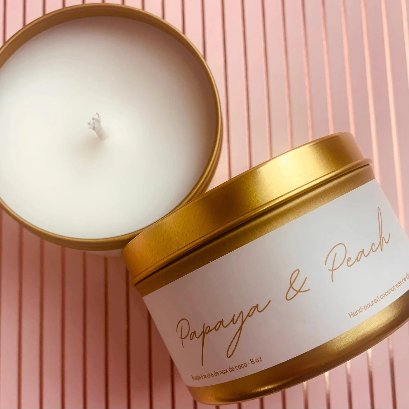 Papaya & Peach candle in a gold tin, featuring coconut wax blend and premium fragrances, on a pink striped background.