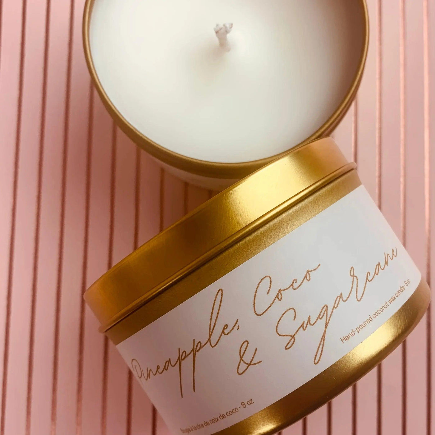 Pineapple, Coco & Sugarcane scented candle in a gold metal tin on a pink striped background.
