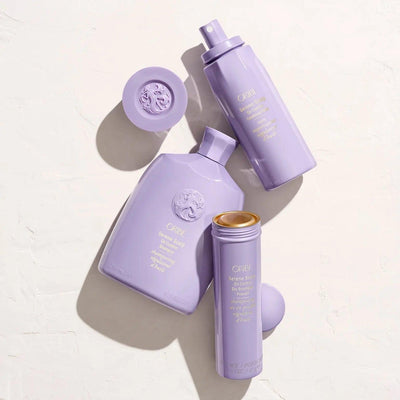 Oribe purple hair care products including a dry shampoo, treatment spray, and styling cream on a light background.