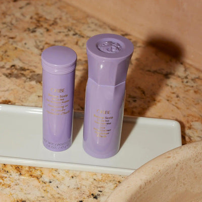 Oribe scalp care products in lavender bottles on a marble countertop for refreshing and revitalizing hair.