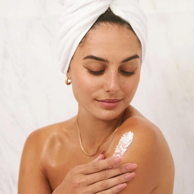 Woman applying Sugar Reef Sugar Scrub on her shoulder, showcasing radiant skin and spa-like relaxation.