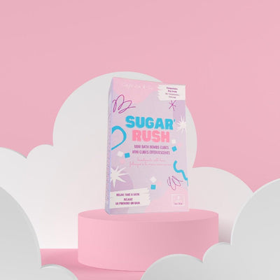 Sugar Rush mini bath bombs packaging displayed on a pastel pink background with whimsical cloud elements.
