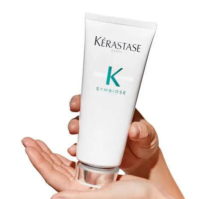 Kérastase Symbiose Fondant Apaisant Essentiel hair conditioner in a hand, perfect for soothing sensitive scalps.