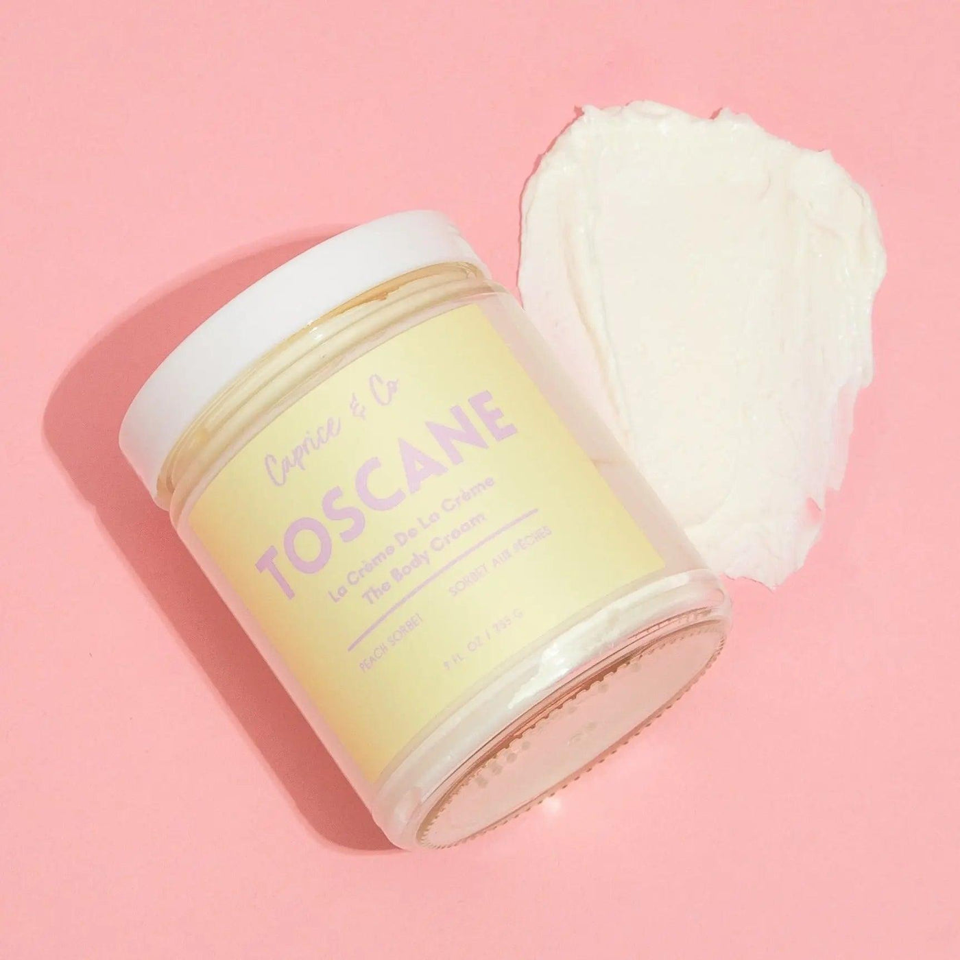 Toscane body cream jar with peach sorbet scent on pink background, showcasing its moisturizing formula and natural ingredients.