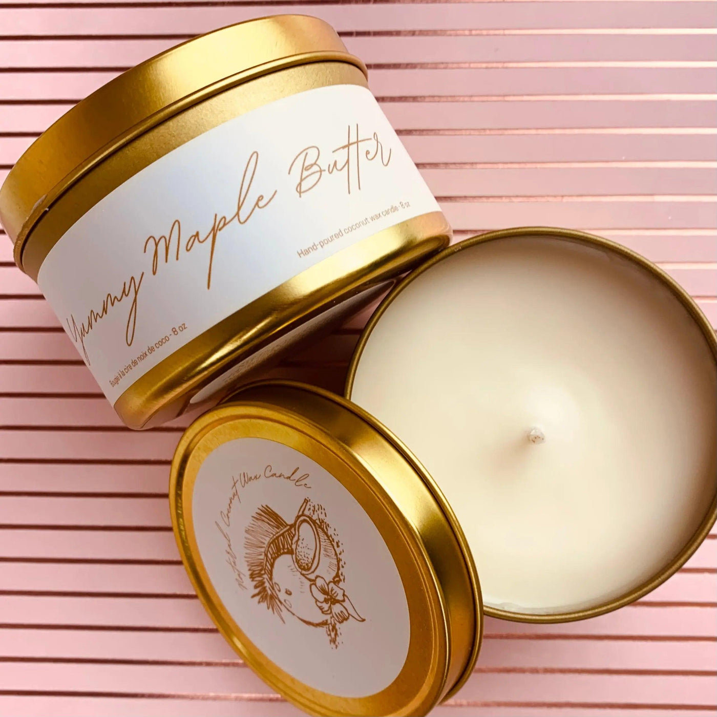 Yummy Maple Butter candle in gold tin with lid, showcasing creamy wax and elegant design on a pink background.